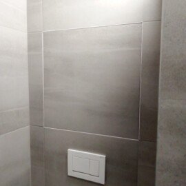 Ovládacie tlačidlo podomietkovej nádržky WC na sivom obklade