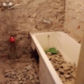 Rozobratá kúpeľňa s vaňou plnou sutiny počas búracích prác