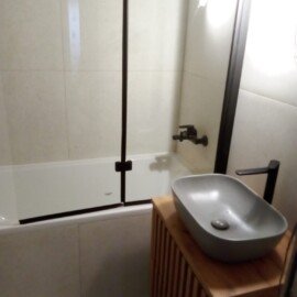 Vaňa so sklenenou zástenou a sivým umývadlom na drevenej skrinke