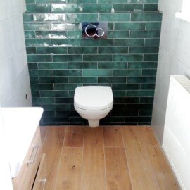 WC so zeleným obkladom, závesnou toaletou a dlažbou v dekore dreva