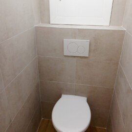 Závesné WC pod bielou skrinkou s béžovým obkladom